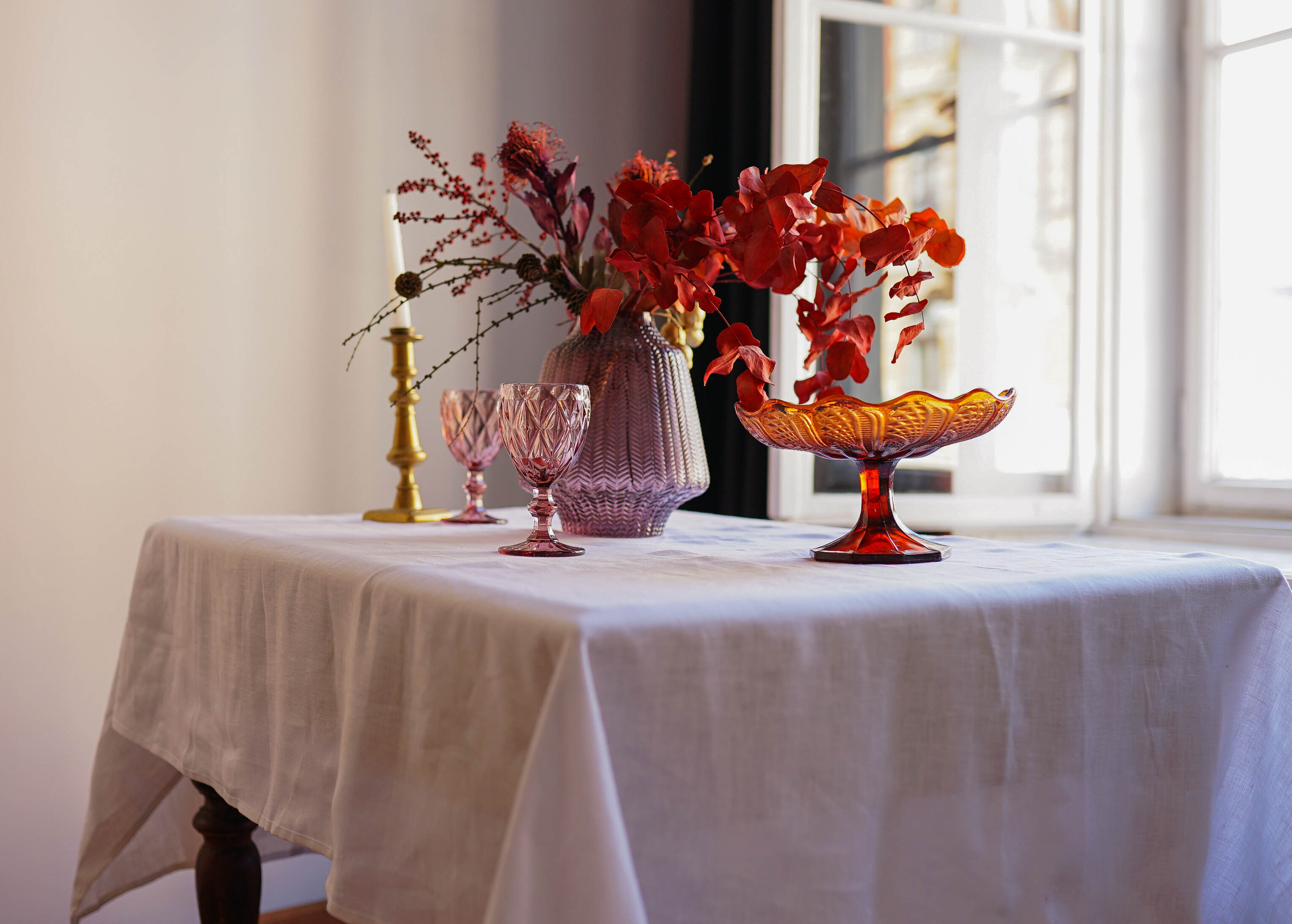 a table with a white table cloth and two vases with red flowers
