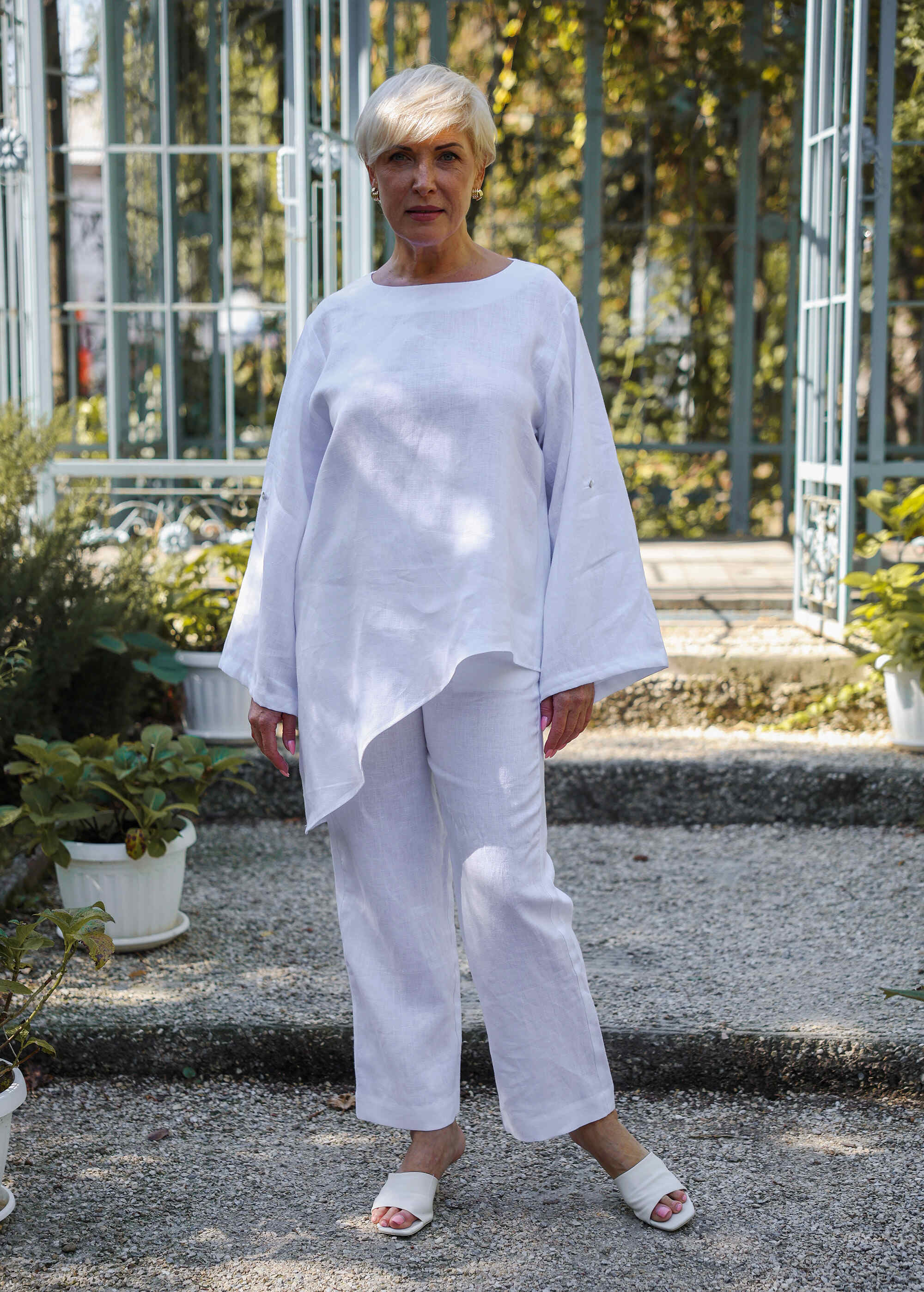 a woman standing in a garden wearing a white outfit